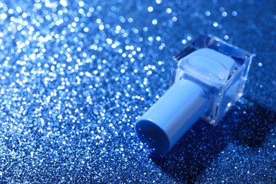 Photo of Nail polish in bottle on blue glitter surface, closeup. Space for text