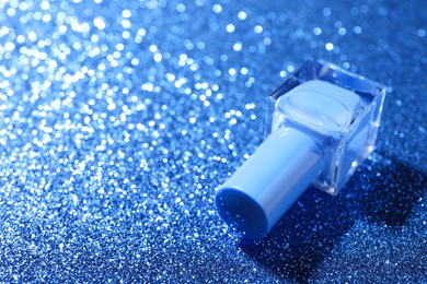 Photo of Nail polish in bottle on blue glitter surface, closeup. Space for text