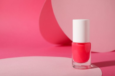 Photo of Nail polish in bottle on pink background, space for text