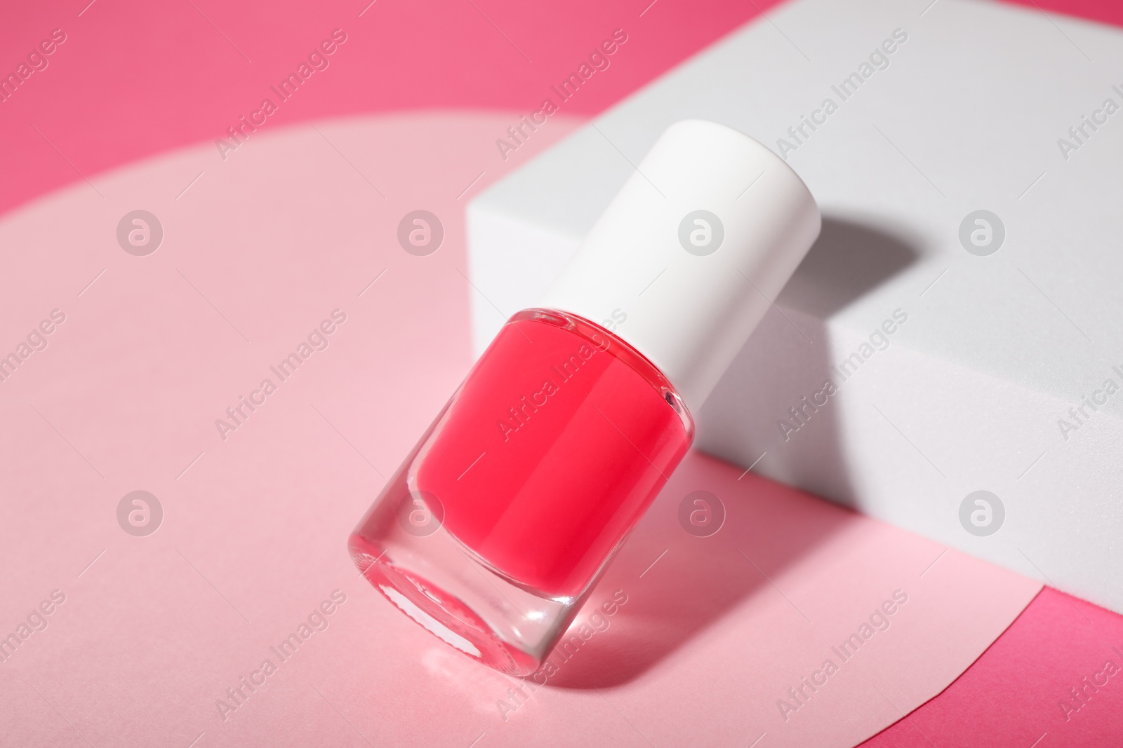 Photo of Stylish presentation of nail polish in bottle on pink background, closeup