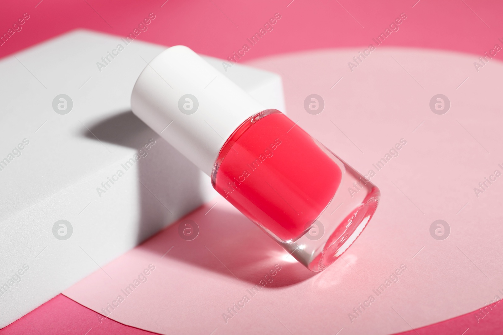 Photo of Stylish presentation of nail polish in bottle on pink background, closeup