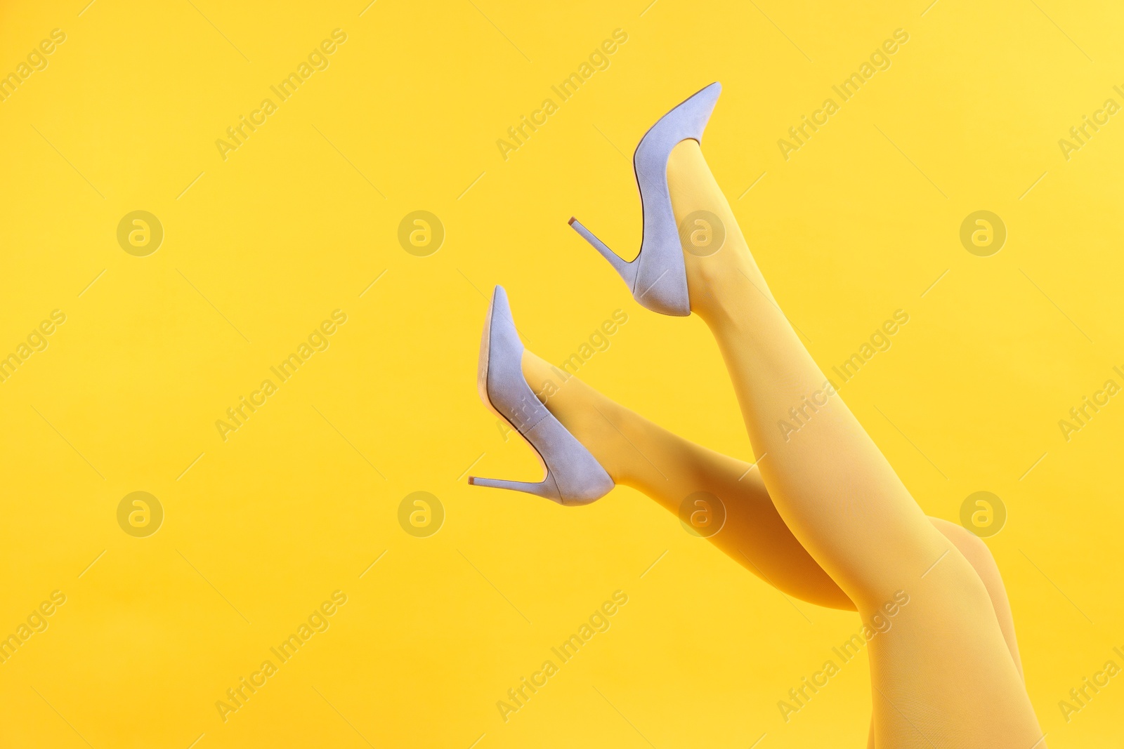 Photo of Woman in light blue shoes showing legs on yellow background, closeup