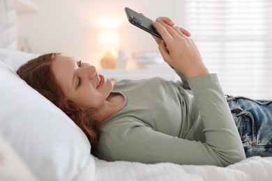 Photo of Beautiful teenage girl using smartphone on bed at home