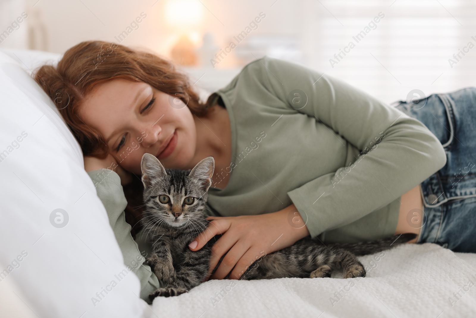 Photo of Beautiful teenage girl with cute cat on bed at home