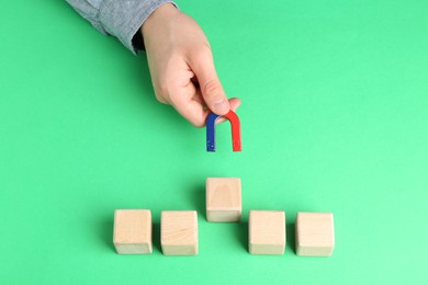 Photo of Man with magnet attracting wooden cubes at green table, closeup