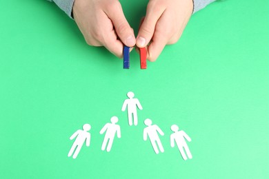 Photo of Man with magnet attracting paper human figures at green table, above view