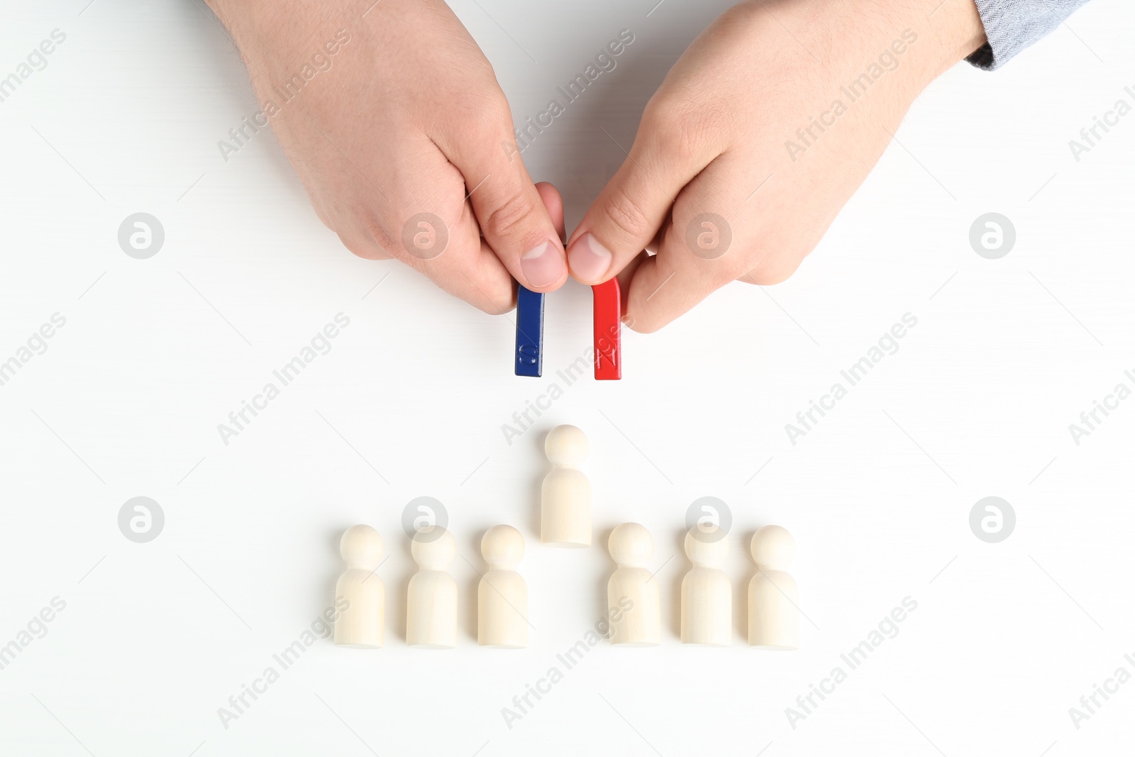 Photo of Man with magnet attracting game pieces at white table, above view