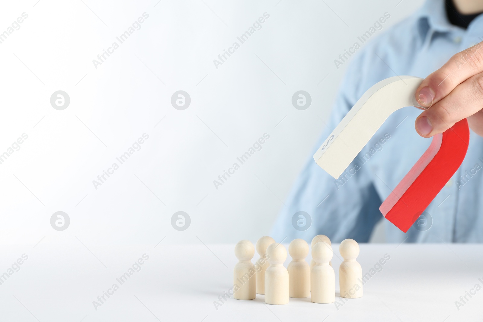 Photo of Man with magnet attracting game pieces at white table, closeup. Space for text