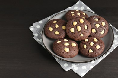 Photo of Delicious chocolate cookies with hazelnuts on black wooden table