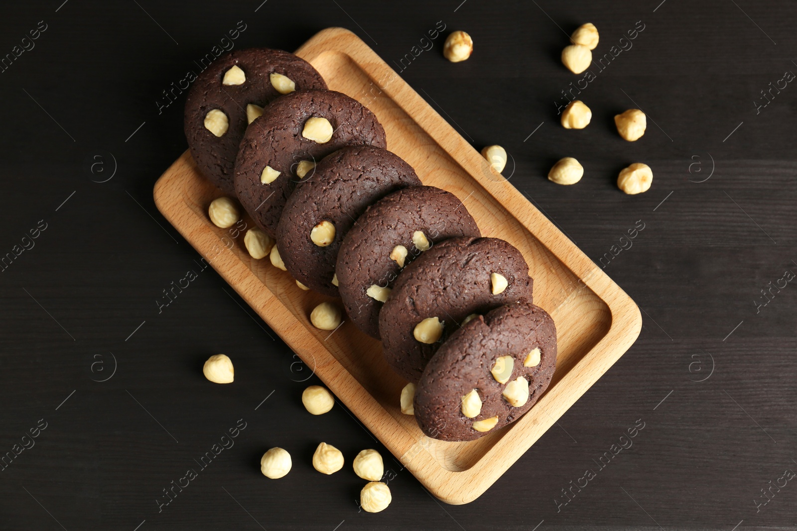 Photo of Delicious chocolate cookies with hazelnuts on black wooden table, flat lay