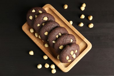 Photo of Delicious chocolate cookies with hazelnuts on black wooden table, flat lay