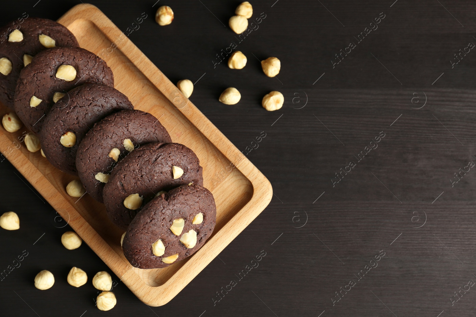 Photo of Delicious chocolate cookies with hazelnuts on black wooden table, flat lay. Space for text