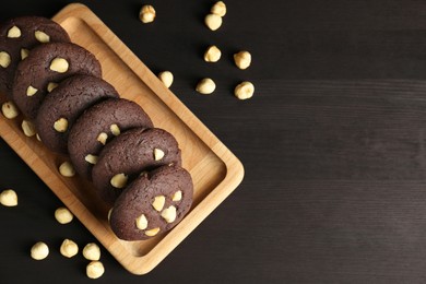 Photo of Delicious chocolate cookies with hazelnuts on black wooden table, flat lay. Space for text