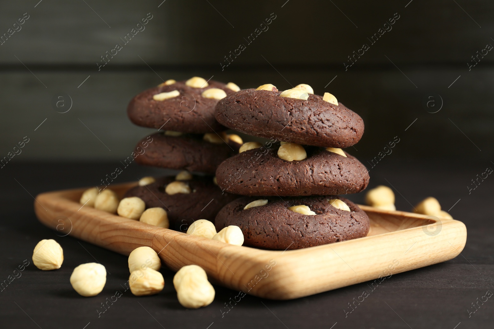 Photo of Delicious chocolate cookies with hazelnuts on black wooden table, closeup