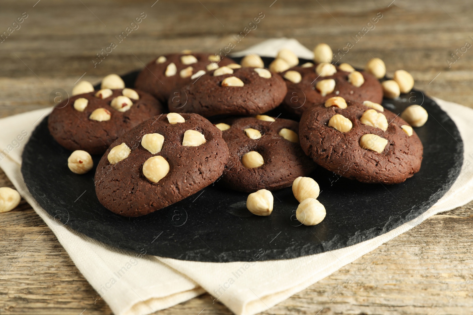 Photo of Tasty chocolate cookies with hazelnuts on wooden table, closeup