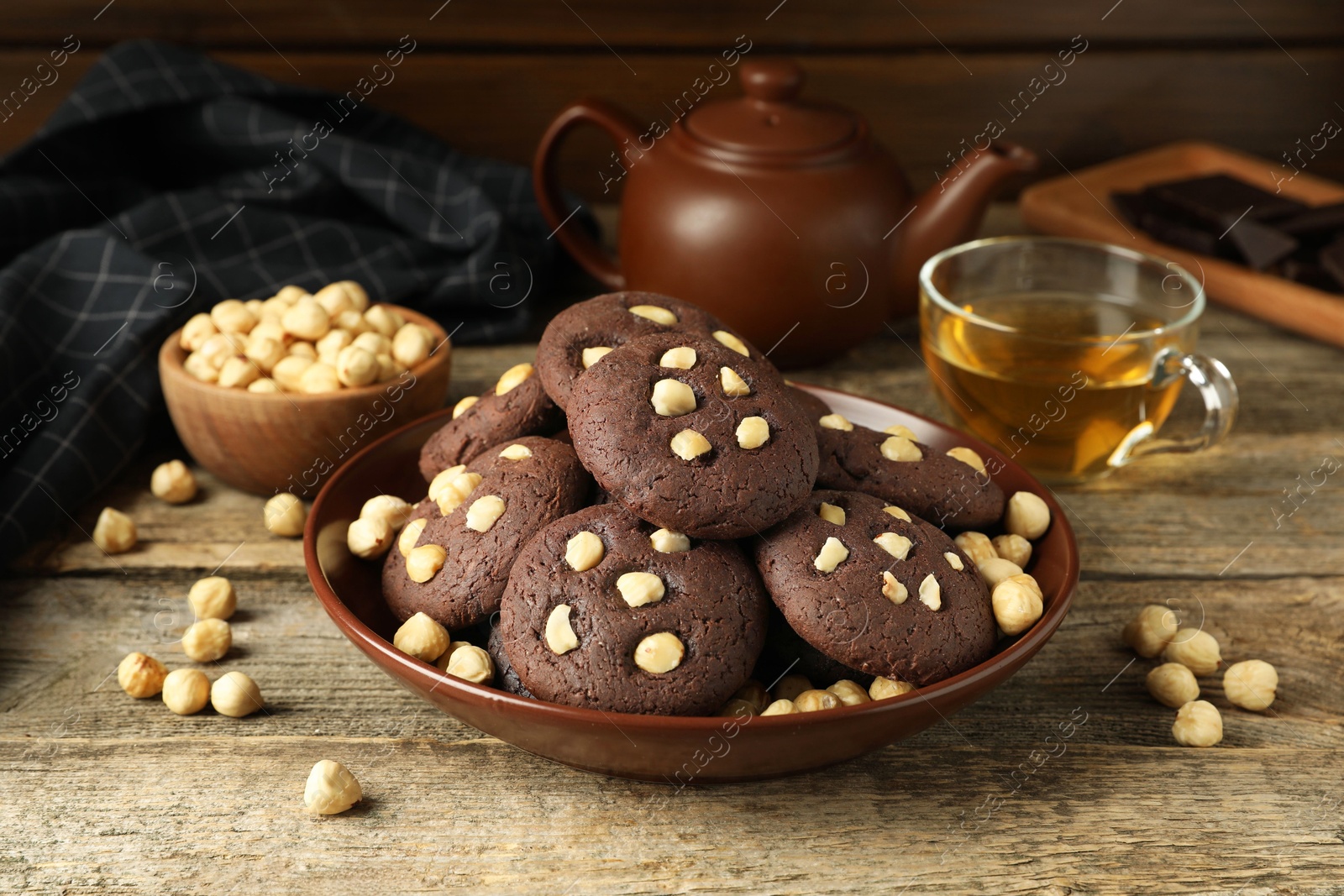 Photo of Tasty chocolate cookies with hazelnuts and tea on wooden table