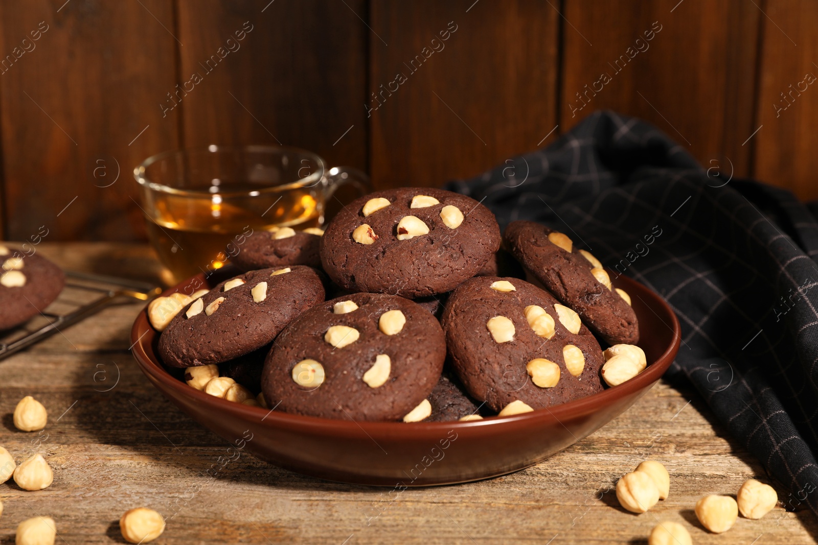 Photo of Tasty chocolate cookies with hazelnuts and tea on wooden table, closeup