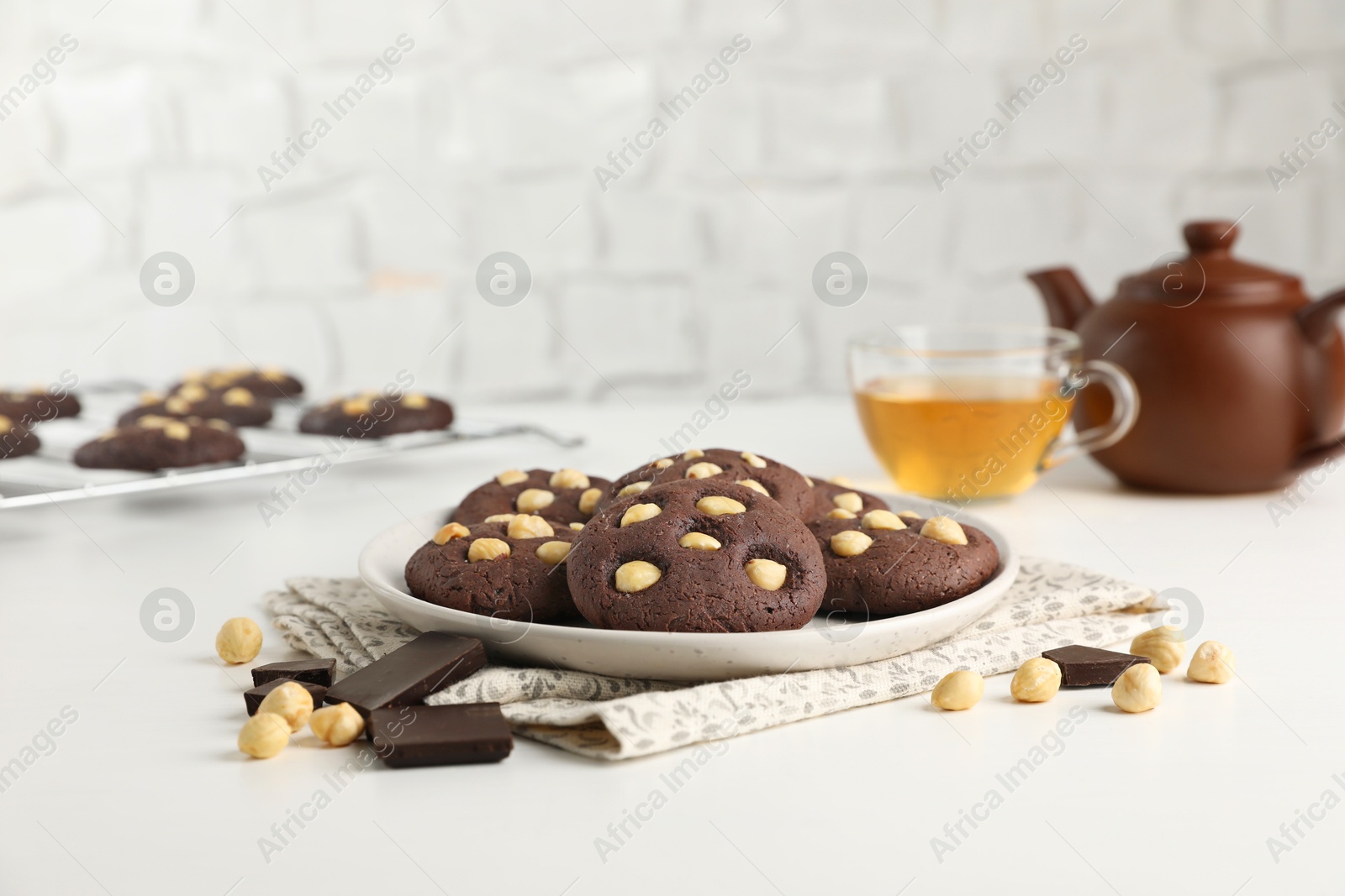 Photo of Tasty chocolate cookies with hazelnuts and tea on white table