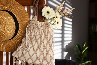 Photo of Handmade macrame shopping bag with flowers and straw hat on wooden chair indoors