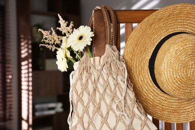 Photo of Handmade macrame shopping bag with flowers and straw hat on wooden chair indoors