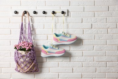 Photo of Handmade macrame shopping bag with flowers and sneakers on white brick wall, space for text