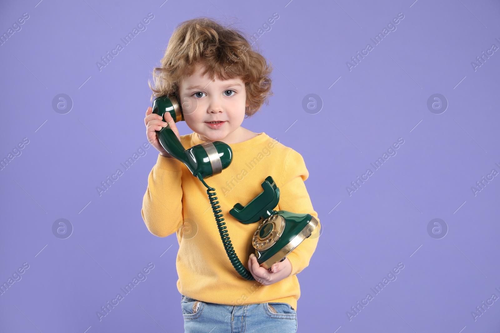 Photo of Cute little boy with old telephone on violet background