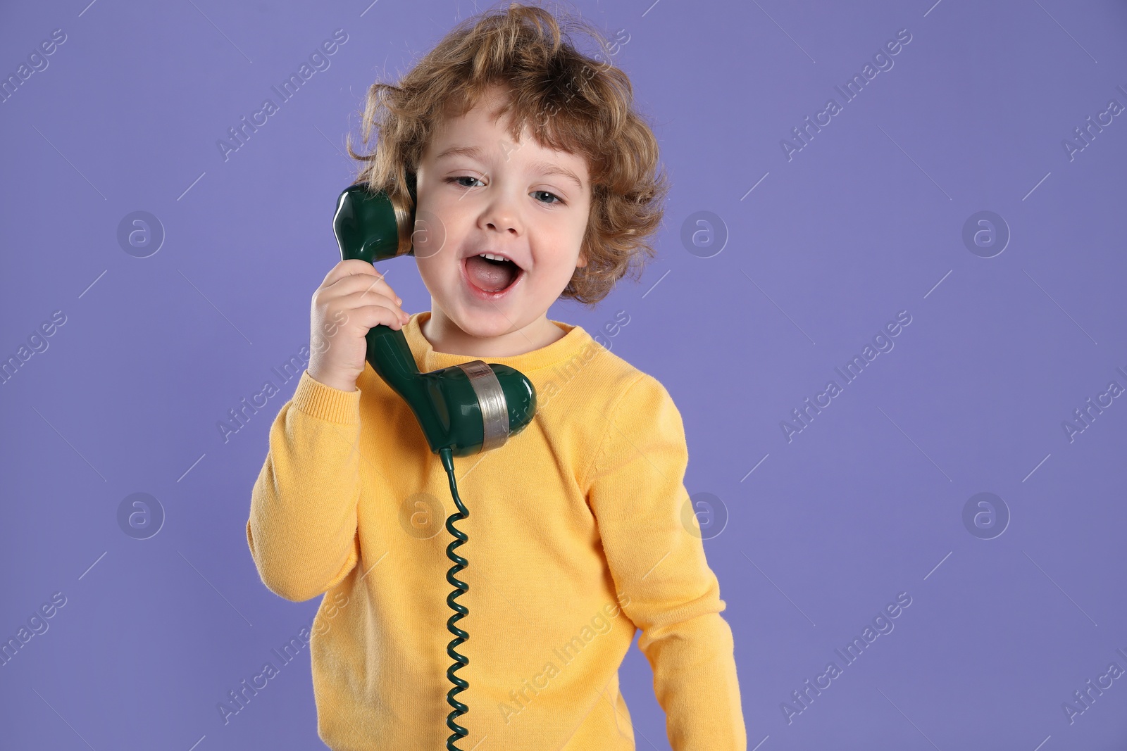 Photo of Cute little boy with telephone handset on violet background