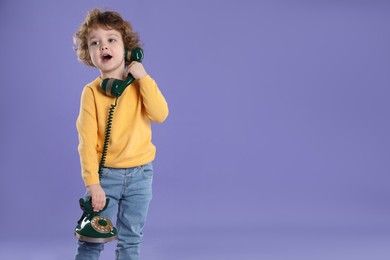 Photo of Cute little boy with old telephone on violet background, space for text