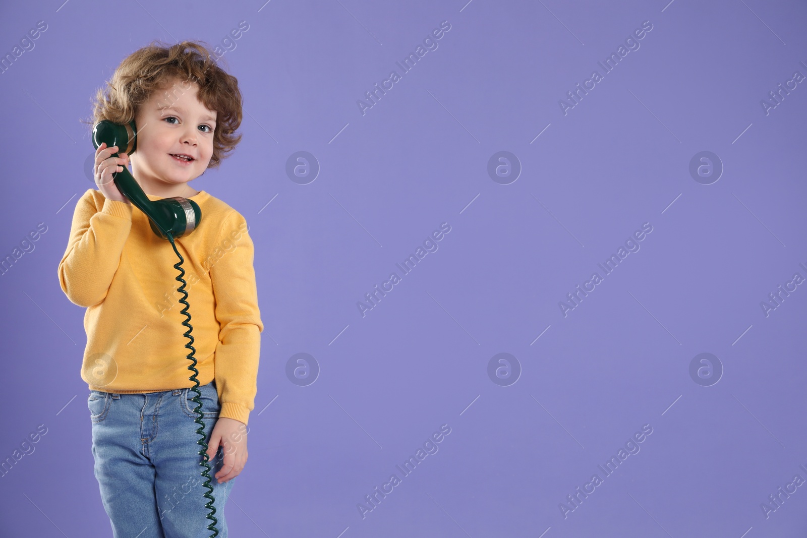 Photo of Cute little boy with telephone handset on violet background, space for text