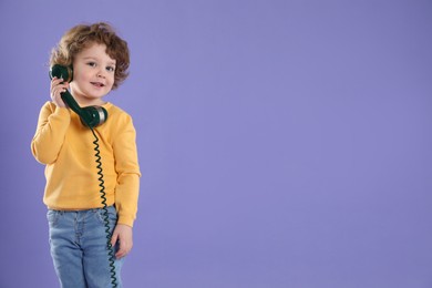 Photo of Cute little boy with telephone handset on violet background, space for text