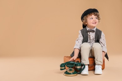 Photo of Cute little boy with old telephone and suitcase on beige background, space for text