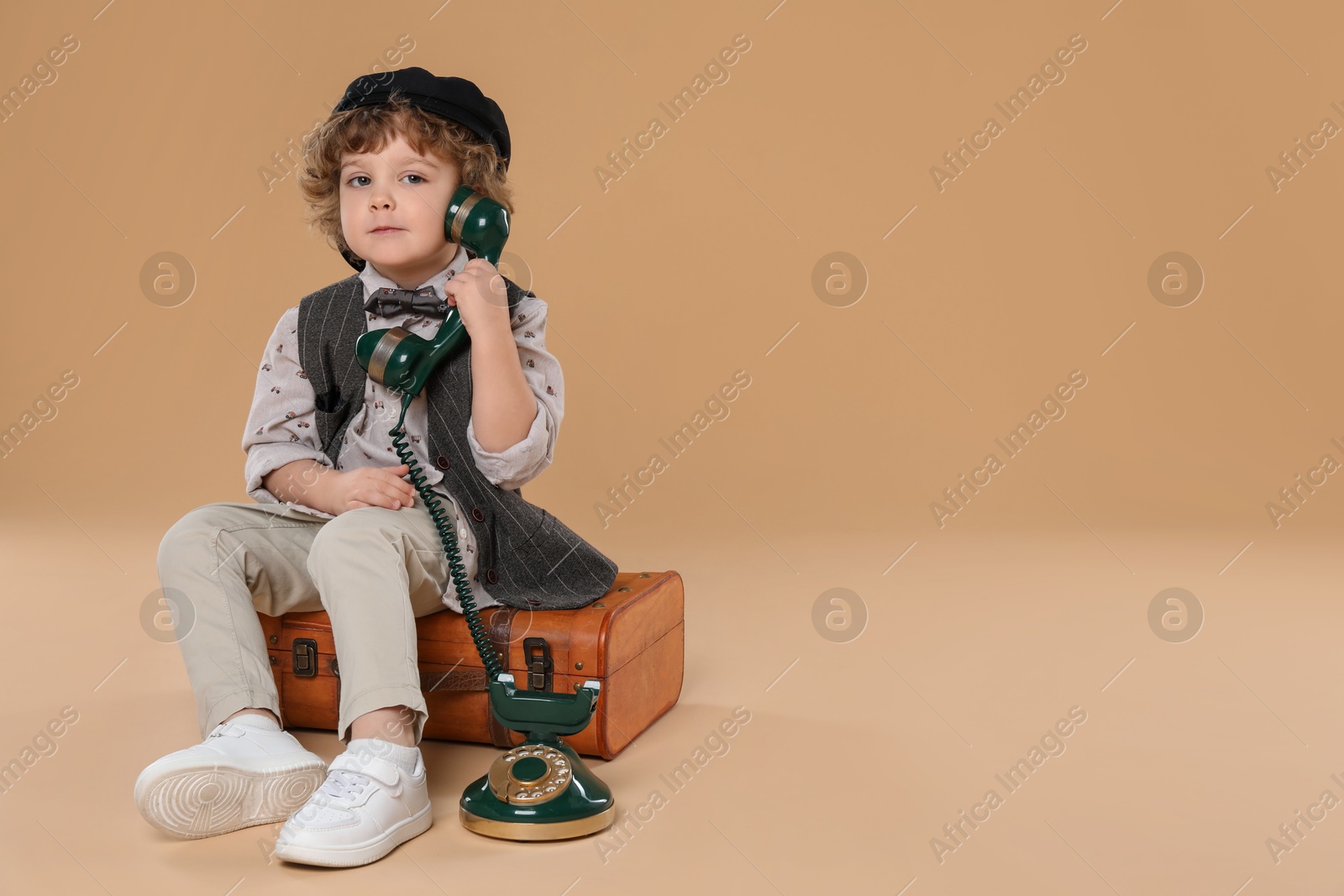 Photo of Cute little boy with old telephone and suitcase on beige background, space for text