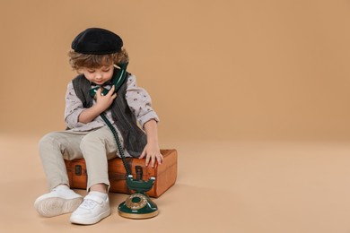 Photo of Cute little boy with old telephone and suitcase on beige background, space for text