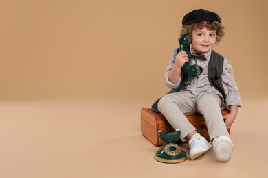 Photo of Cute little boy with old telephone and suitcase on beige background, space for text