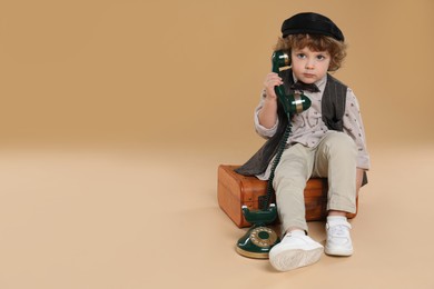 Photo of Cute little boy with old telephone and suitcase on beige background, space for text