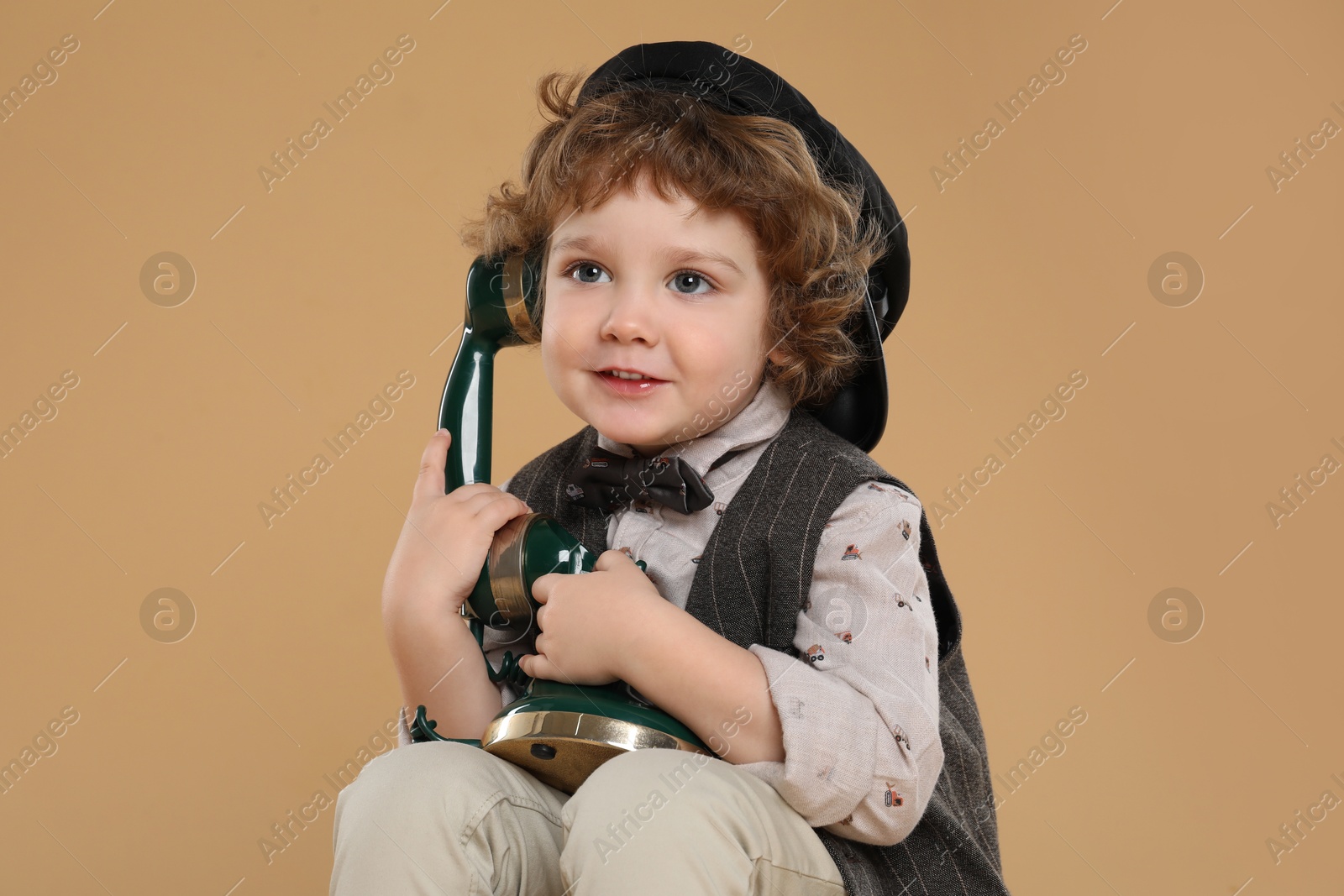 Photo of Cute little boy with old telephone on beige background