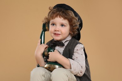 Cute little boy with old telephone on beige background