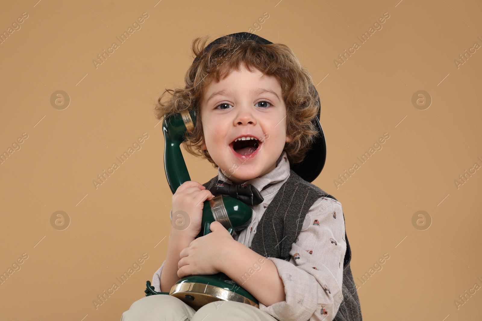 Photo of Cute little boy with old telephone on beige background