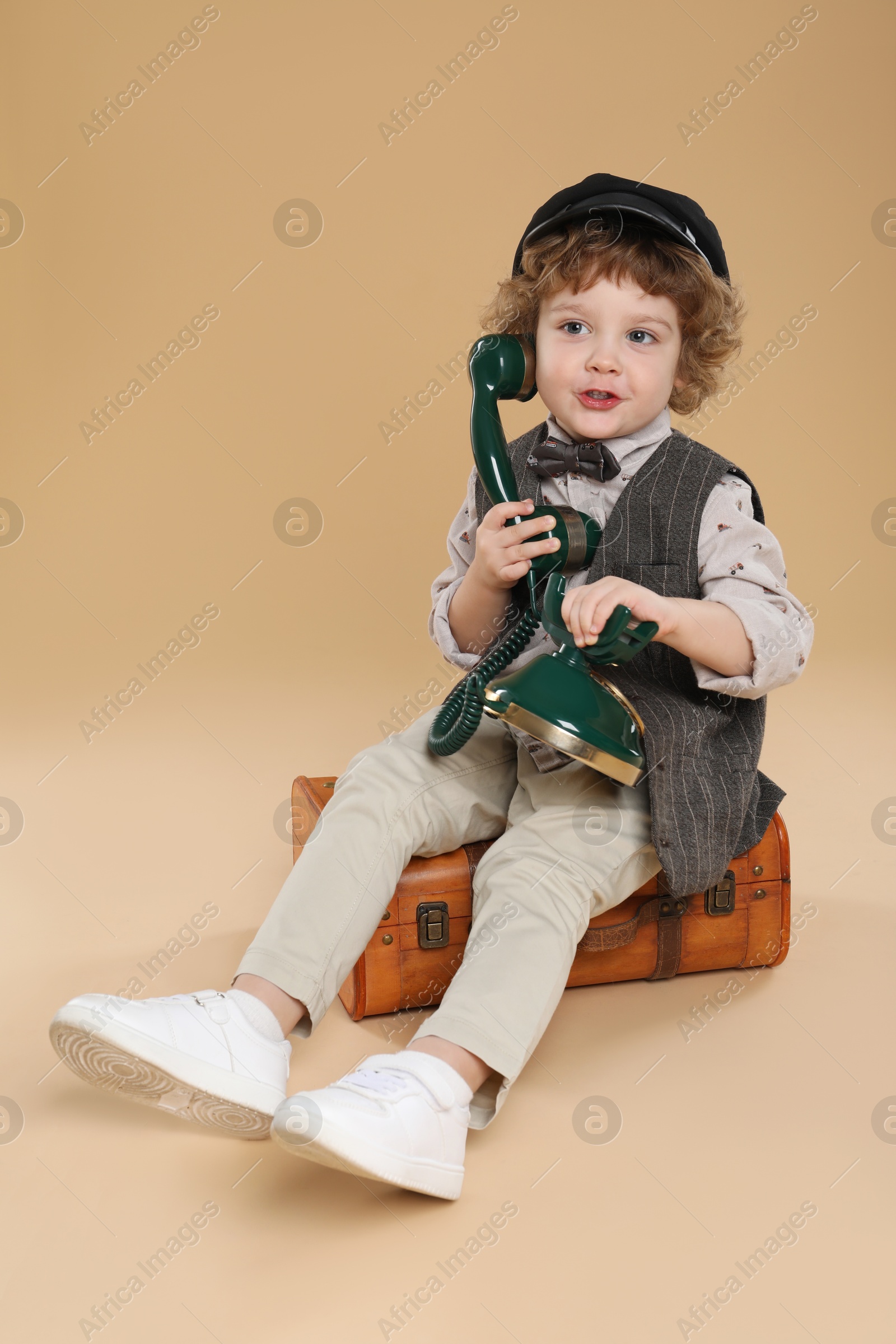 Photo of Cute little boy with old telephone and suitcase on beige background