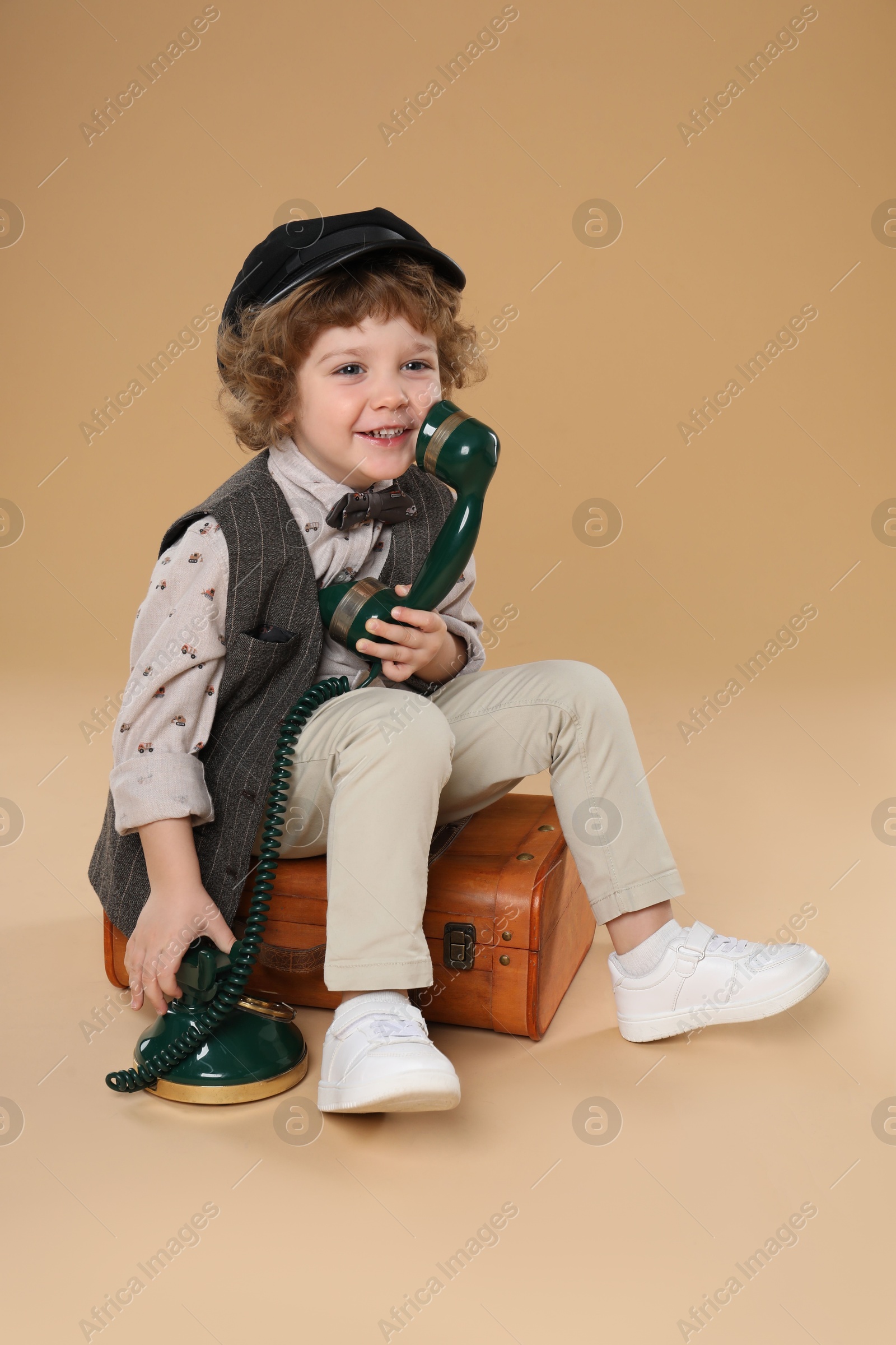 Photo of Cute little boy with old telephone and suitcase on beige background