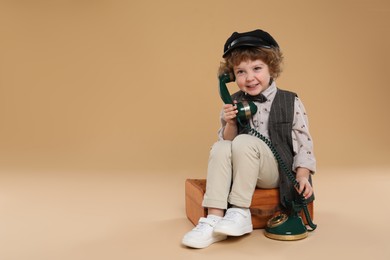 Photo of Cute little boy with old telephone and suitcase on beige background, space for text