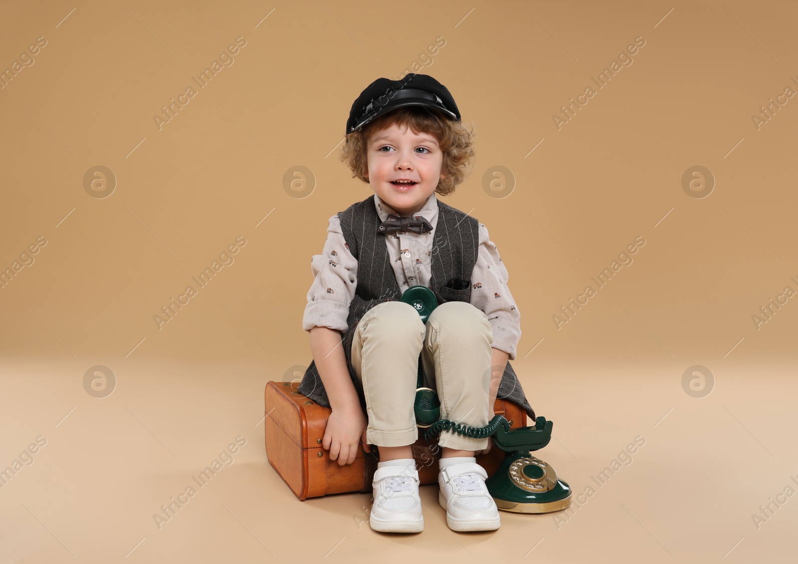 Photo of Cute little boy with old telephone and suitcase on beige background