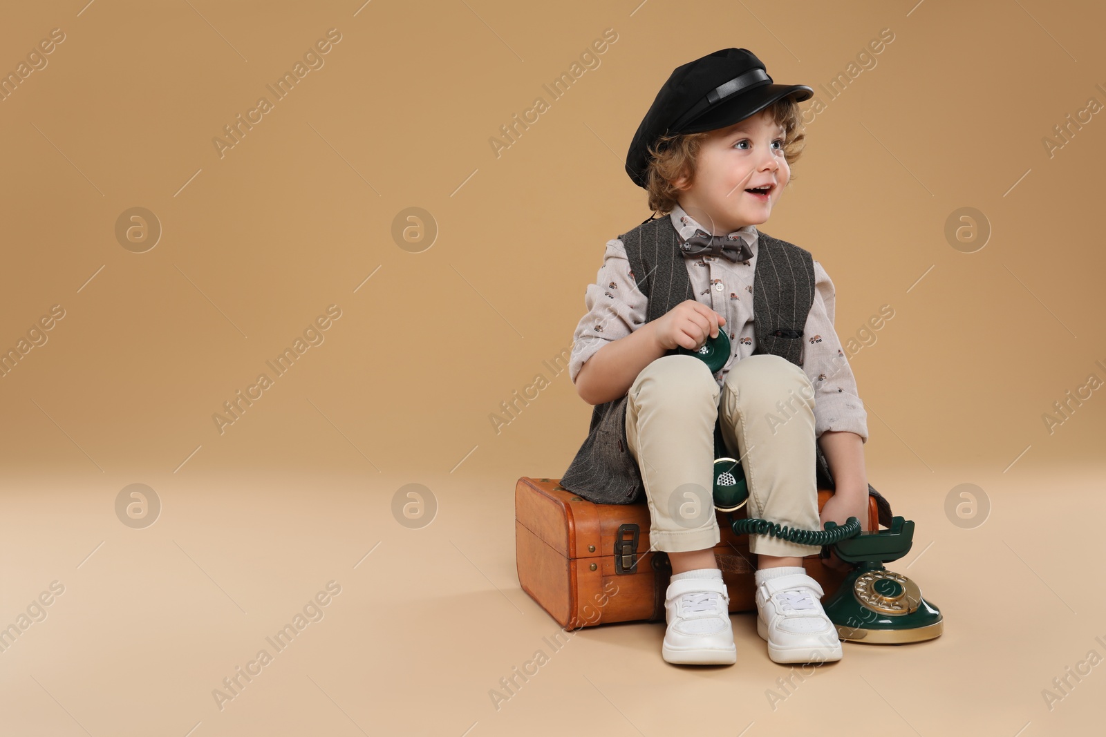 Photo of Cute little boy with old telephone and suitcase on beige background, space for text