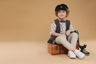 Photo of Cute little boy with old telephone and suitcase on beige background, space for text