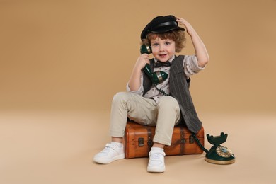 Photo of Cute little boy with old telephone and suitcase on beige background, space for text