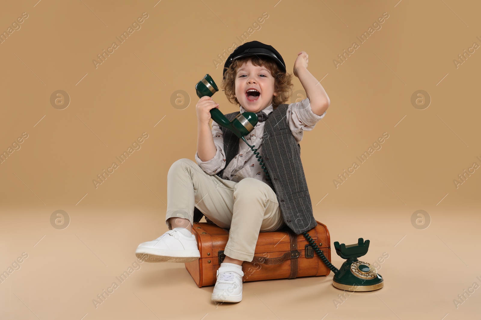 Photo of Cute little boy with old telephone and suitcase on beige background