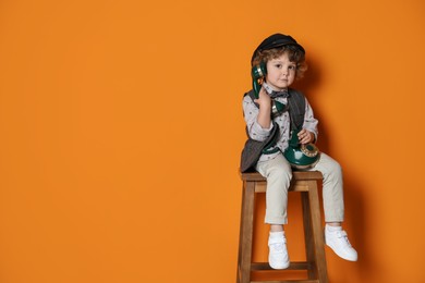 Photo of Cute little boy with old telephone on stool against orange background, space for text