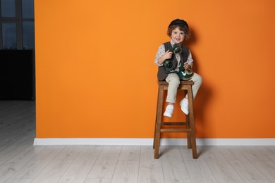 Photo of Cute little boy with old telephone on stool near orange wall, space for text