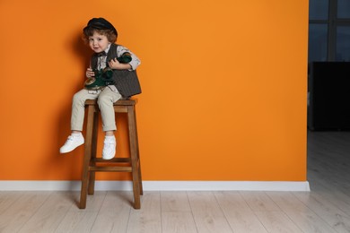 Photo of Cute little boy with old telephone on stool near orange wall, space for text