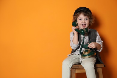 Photo of Cute little boy with old telephone on stool against orange background, space for text